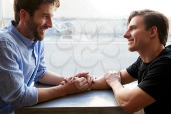 Loving Male Gay Couple Sitting At Table In Coffee Shop Holding Hands