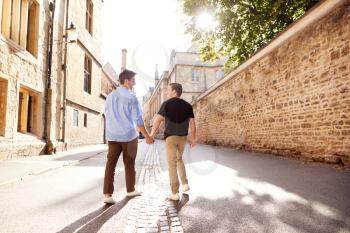 Rear View Of Male Gay Couple On Vacation Holding Hands Walking Along City Street