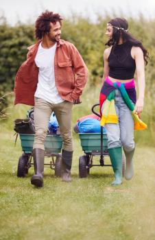 Young Couple Pulling Trolley Filled With Camping Equipment Through Field To Music Festival