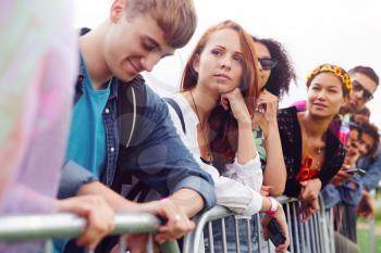 Group Of Young Friends Waiting Behind Barrier At Entrance To Music Festival Site