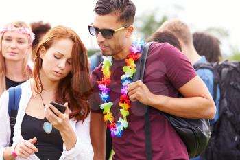 Couple Looking At Mobile Phone As They Wait Behind Barrier At Entrance To Music Festival Site