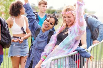 Portrait Of Female Friends Waiting Behind Barrier At Entrance To Music Festival Site