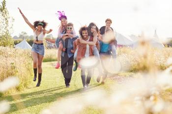 Group Of Friends Walking Back To Tent After Outdoor Music Festival With Men Giving Women Piggybacks