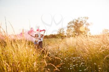 Two Female Friends Camping At Music Festival Running Through Field With Smoke Flare