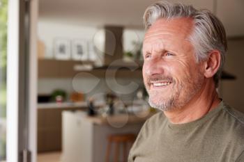 Smiling Senior Man Standing And Looking Out Of Kitchen Door