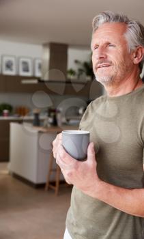 Senior Man Standing And Looking Out Of Kitchen Door Drinking Coffee