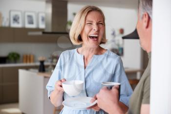 Senior Couple Standing At Home In Kitchen Drinking Morning Coffee Together