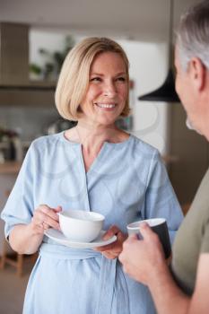 Senior Couple Standing At Home In Kitchen Drinking Morning Coffee Together