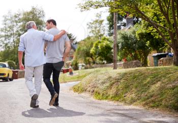 Rear View Of Senior Father With Adult Son Talking As They Walk Along Country Road Together