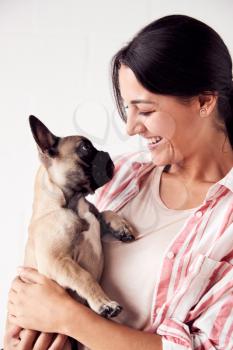 Studio Shot Of Smiling Young Woman Holding Affectionate Pet French Bulldog Puppy