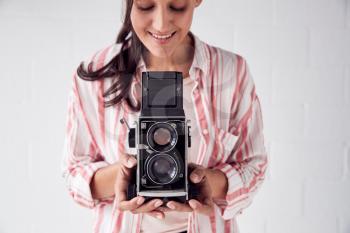 Female Photographer With Vintage Medium Format Camera On Photo Shoot Against White Studio Backdrop