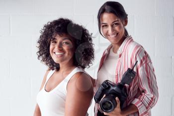 Portrait Of Smiling Female Photographer Holding Camera With Model In Studio Portrait Session