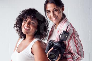 Portrait Of Smiling Female Photographer Holding Camera With Model In Studio Portrait Session