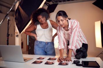 Photographer With Female Client Editing Images From Portrait Photo Shoot In Studio