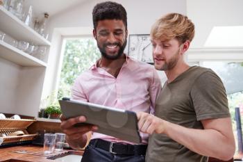 Male Gay Couple Using Digital Tablet At Home In Kitchen Together