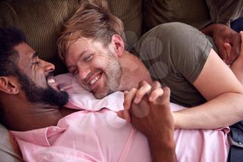 Loving Male Gay Couple Relaxing Lying On Sofa At Home Hugging