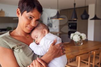 Loving Mother Holding Sleeping 3 Month Old Baby Daughter In Kitchen At Home