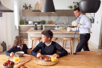 Children Wearing School Uniform Eating Breakfast As Father Gets Ready For Work