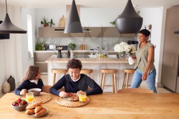 Mother In Kitchen Helping Children With Breakfast Before Going To School