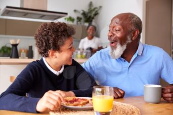 Grandparents Sitting In Kitchen With Grandson Eating Breakfast Before Going To School