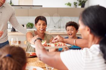 Father Serving As Multi-Generation Mixed Race Family Eat Meal Around Table At Home Together