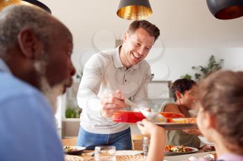 Father Serving As Multi-Generation Mixed Race Family Eat Meal Around Table At Home Together