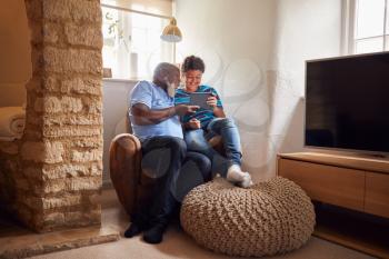 Grandfather Sitting In Chair With Grandson Watching Movie On Digital Tablet Together
