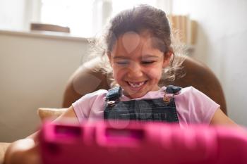 Girl Sitting In Armchair At Home Playing With Digital Tablet