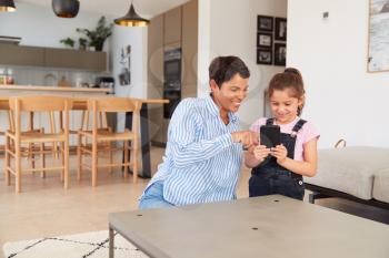 Mother And Daughter Looking At Mobile Phone Together At Home