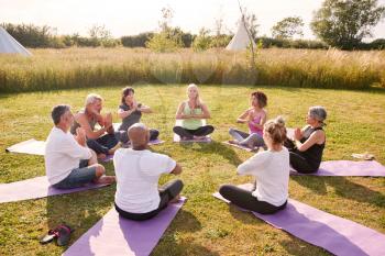 Group Of Mature Men And Women In Class At Outdoor Yoga Retreat Sitting Circle Meditating