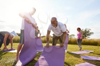 Group Of Mature Men And Women Rolling Up Exercise Mats At End Of Outdoor Yoga Class