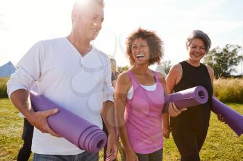 Group Of Mature Men And Women With Exercise Mats At End Of Outdoor Yoga Class