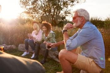 Group Of Mature Friends Sitting Around Fire As They Drink Wine At Outdoor Campsite