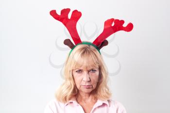 Studio Shot Of Unhappy Mature Woman Wearing Dressing Up Reindeer Antlers Against White Background