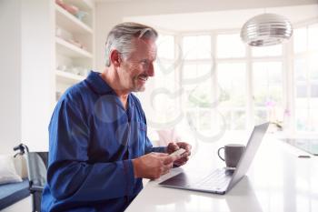 Mature Man In Wheelchair Looking Up Information About Medication Online Using Laptop