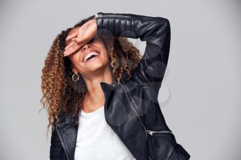 Studio Shot Of Happy Young Woman Wearing Leather Jacket Covering Face With Hand