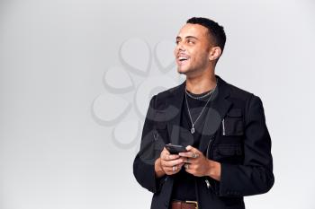 Studio Shot Of Causally Dressed Young Man Using Mobile Phone Looking Off Camera