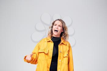Studio Shot Of Angry Woman Shouting Off Camera Against White Background