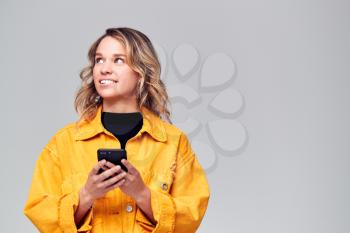 Studio Shot Of Causally Dressed Young Woman Using Mobile Phone Looking Off Camera