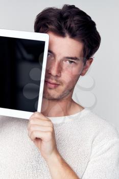 Studio Portrait Of Worried Young Man Covering Face With Digital Tablet