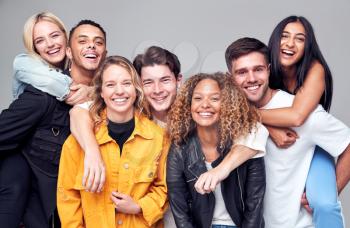 Group Studio Shot Of Young Multi-Cultural Friends Giving Each Other Piggybacks And Smiling At Camera