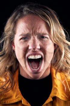 Studio Portrait Of Angry Woman Shouting At Camera Against Black Background
