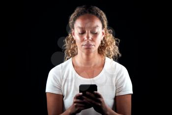 Studio Shot Of Unhappy Woman Holding Mobile Phone Being Bullied Online