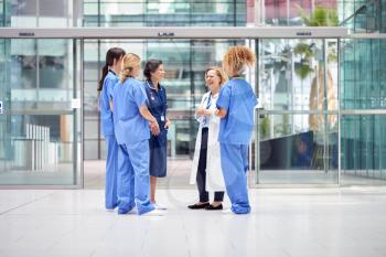 Female Medical Team Having Informal Meeting Standing In Lobby Of Modern Hospital Building