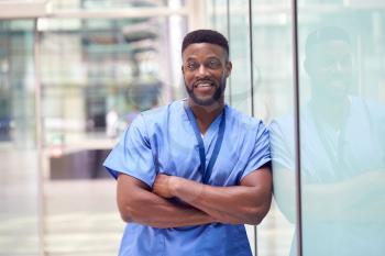 Portrait Of Male Doctor Wearing Scrubs Standing In Modern Hospital Building