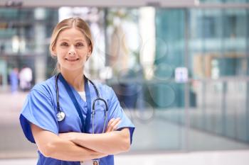 Portrait Of Female Doctor With Stethoscope Wearing Scrubs Standing In Modern Hospital Building