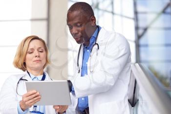Male And Female Doctors Having Informal Meeting In Modern Hospital Looking At Digital Tablet