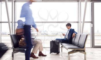 Businessman Sitting In Busy Airport Departure Lounge Using Mobile Phone