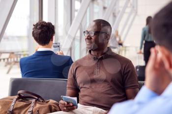 Male Passenger Sitting In Airport Departure Lounge Holding Passport