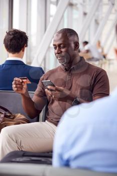 Businessman Sitting In Airport Departure Lounge Shopping Online Using Mobile Phone